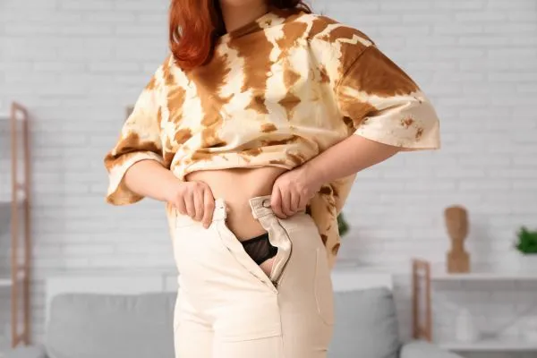 Image of woman trying to do her trousers up after pregnancy weight gain Gloucestershire